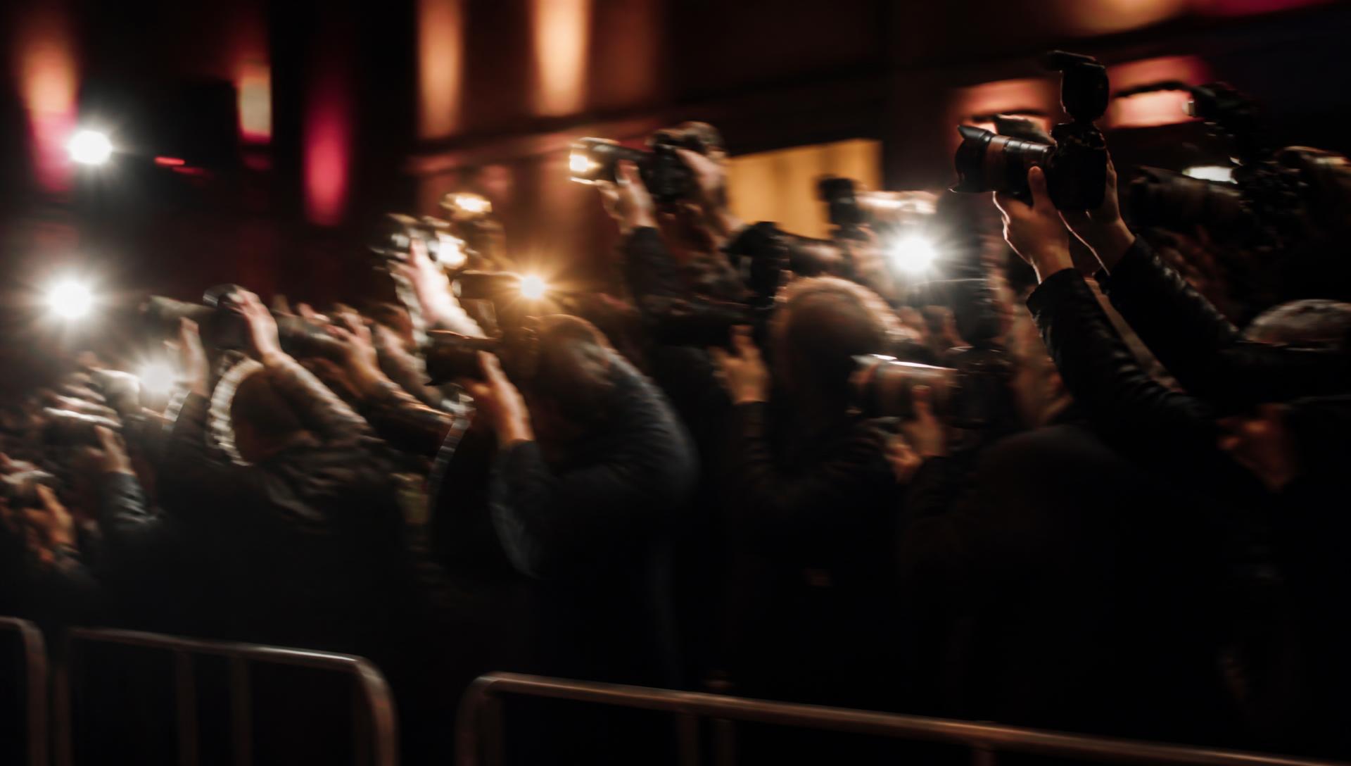 Press photographers at a premiere, motion-blurred under flashlight